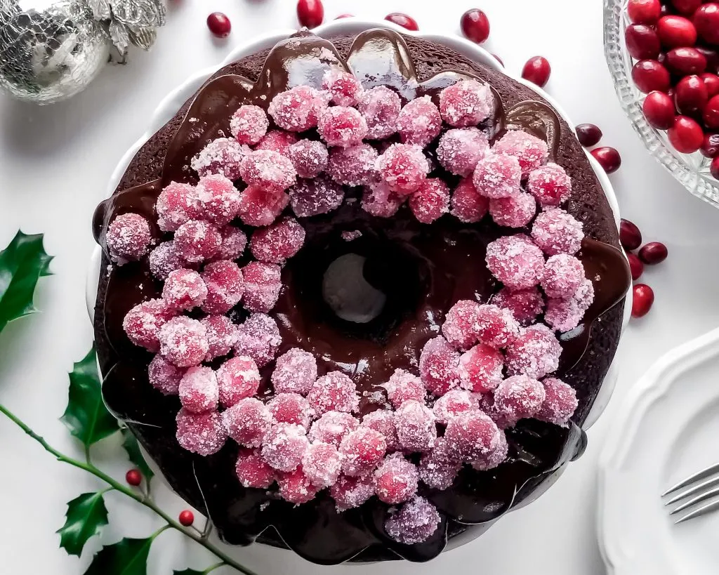 Vegan Cranberry Chocolate Fudge Bundt Cake with Ganache and Sugared Cranberries, view top down and table decoarted with Christmas ornaments and holly