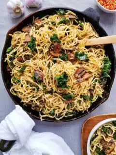 Cast iron skillet filled with spaghetti noodles, seared mushrooms and kale