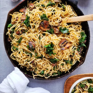 Cast iron skillet filled with spaghetti noodles, seared mushrooms and kale