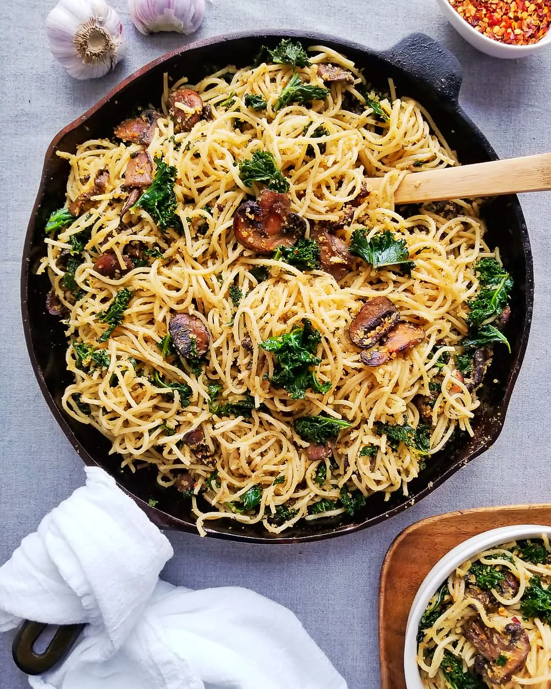 Cast iron skillet filled with spaghetti noodles, seared mushrooms and kale