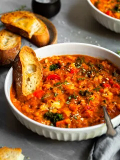 White bowl of roasted vegetable stew with red lentils and tomatoes, served with a thick slice of toast