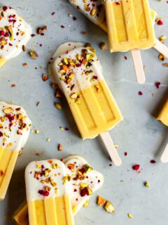 Mango Lassi Ice Pops on marble surface dipped in yogurt and sprinkled with chopped pistacios and freeze dried raspberries