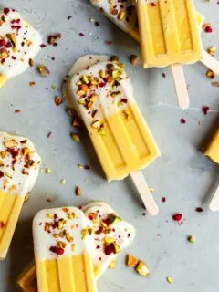 Mango Lassi Ice Pops on marble surface dipped in yogurt and sprinkled with chopped pistacios and freeze dried raspberries
