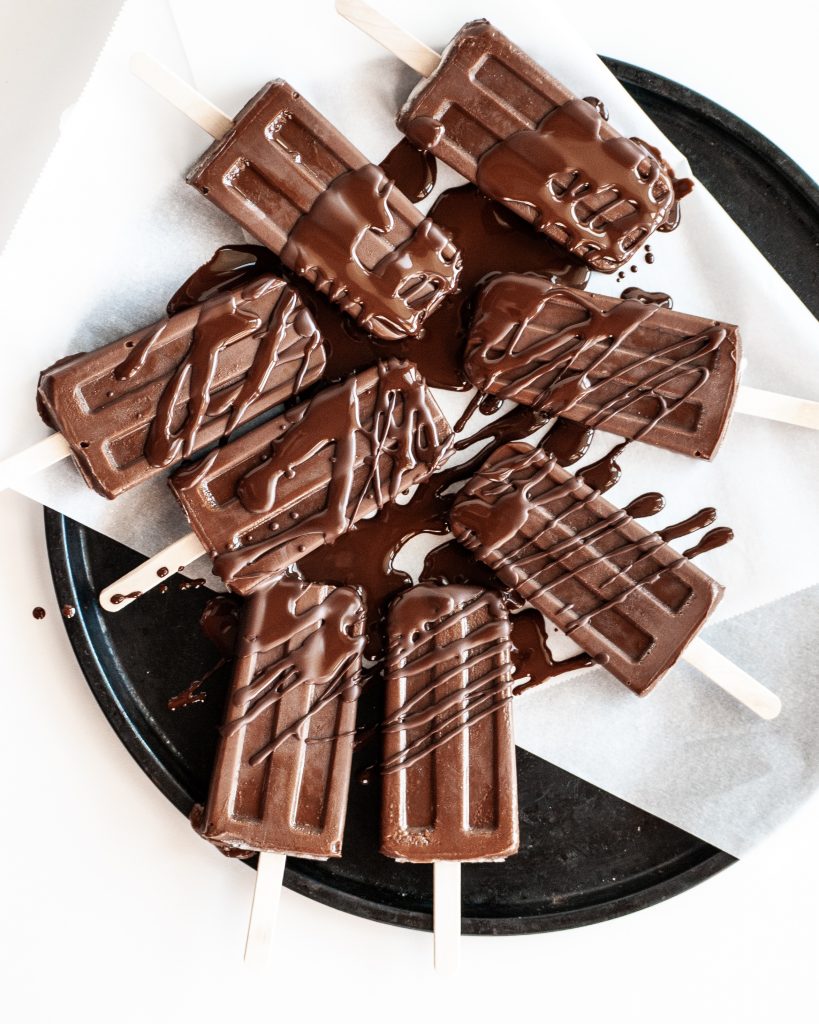 A black round platter lined with white parchment paper containing 8 chocolate fudge ice pops. 