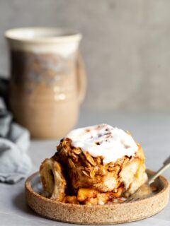 A glazed cinnamon roll on a plate with a cup of coccee in the background