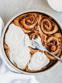 Vegan Apple Cinnamon Rolls being slathered with Vanilla Glaze