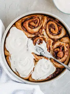 Vegan Apple Cinnamon Rolls being slathered with Vanilla Glaze