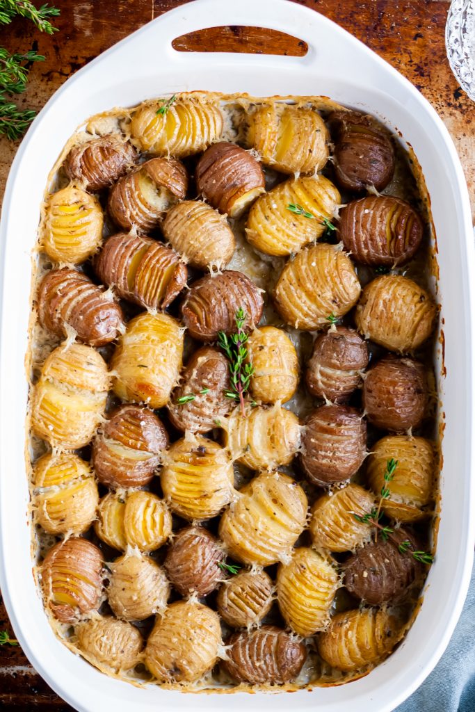 white baking dish filled with baby hasselback potatoes in a vegan cream sauce