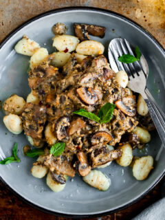 Plate filled with Pan-Fried Gnocchi and Seared Mushrooms in a Cashew Butter Pesto Sauce served with chilli flakes, fresh basil
