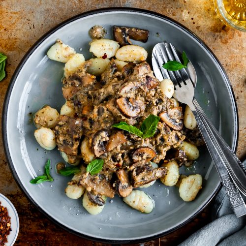 Plate filled with Pan-Fried Gnocchi and Seared Mushrooms in a Cashew Butter Pesto Sauce served with chilli flakes, fresh basil