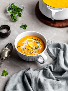 Creamy Curried Carrot, Ginger and Red Lentil Soup served in a large cup with ingredients in background