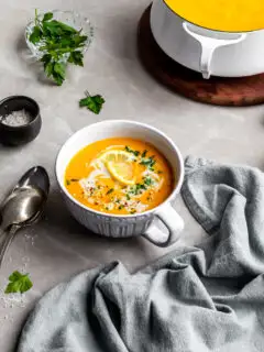 Creamy Curried Carrot, Ginger and Red Lentil Soup served in a large cup with ingredients in background