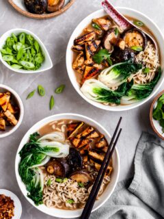 flatlay of 2 bowls of mushroom miso ramen and several bowls of garnishes
