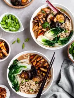 flatlay of 2 bowls of mushroom miso ramen and several bowls of garnishes