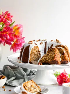 Vegan Hummingbord Cake with Vanilla Glaze sliced and sitting beside a vase of pink tulips