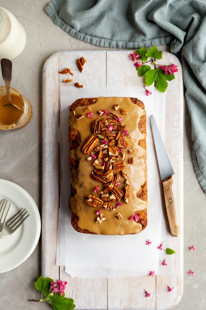 Vegan Carrot Spice Loaf with Maple Glaze garnished with pecans and fresh pink currant blossoms