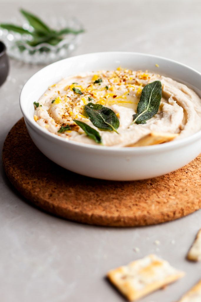 Lemon Sage White Bean Dip garnished with fried sage leaves and served with crackers
