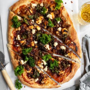 Vegan Caramelized Onion, Sausage and Kale Pizza with Almond Ricotta sliced and served with a glass of beer