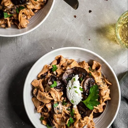 Mushroom Stroganoff served in white bowls, arnished with almond ricotta and parsley