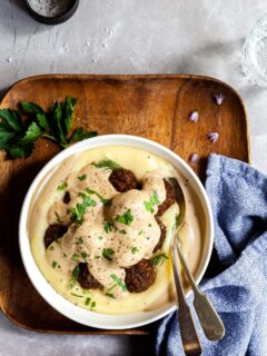 Vegan Swedish Meatballs in a bowl over mashed potatoes, covered in gravy alongside a blue napkin