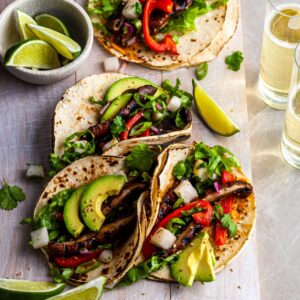 Vegan Korean Tacos served on a white wood board with a side of limes and a glass of beer