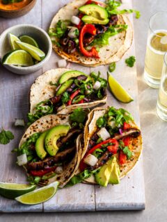 4 Korean Mushroom Tacos on a white serving board served with lime wedges, Gochujang crema and beer