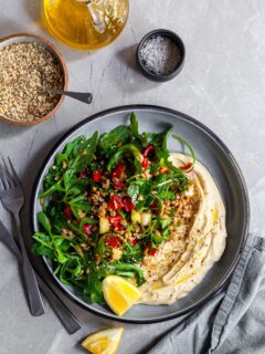 Looking down on a bowl of farro salad over hummus, served with lemon wedges and dukkah
