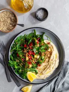 Looking down on a bowl of farro salad over hummus, served with lemon wedges and dukkah