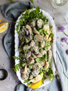 Potato salad on a white platter, garnished with fresh lemons and chive blossoms