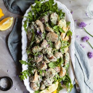 Potato salad on a white platter, garnished with fresh lemons and chive blossoms
