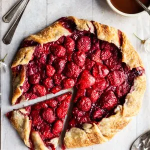 Fresh baked strawberry galette with one slice cut beside a white bowl of chocolate hazelnut sauce