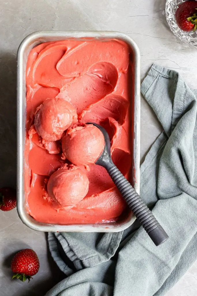 Strawberry Rhubarb Sorbet in loaf pan with 3 scoops sitting ready to be served beside a few fresh strawberries