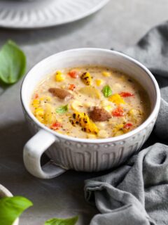 Large mug of chowder on a counter with basil leaves and another bowl in the background
