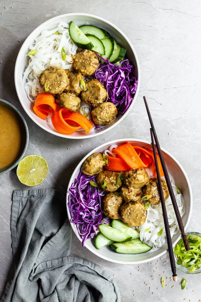 Two white Thai noodles bowls with chickpea meatballs and fresh vibrant veggies, served with a side bowl of yellow curry sauce