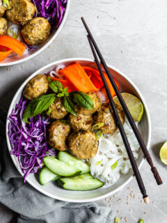 White bowl and chopsticks with rice noodles, chcikpea balls covered in yellow curry sauce, and raw veggies