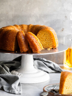 Sliced rum bundt cake on cake stand and a slice on a plate in the foreground