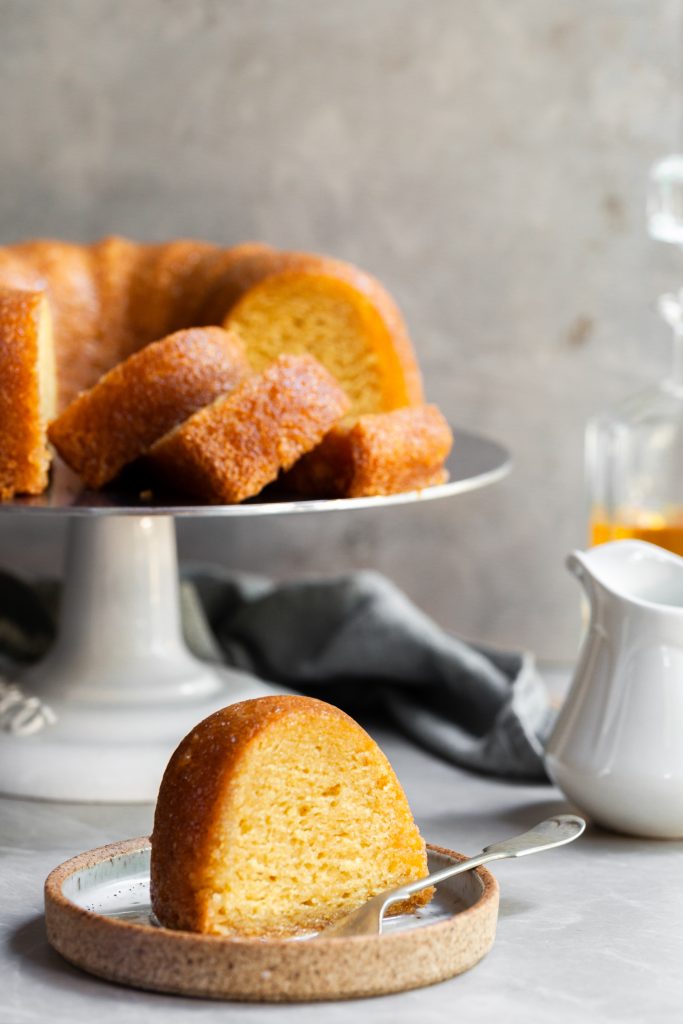 Slice of rum bundt cake on a small plate with the partly sliced bundt cake in the background