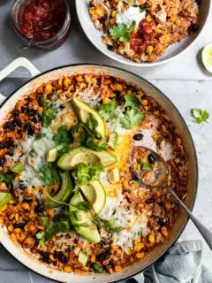 White skillet filled with rice, beans and corn with a serving just removed and spooned into a white bowl