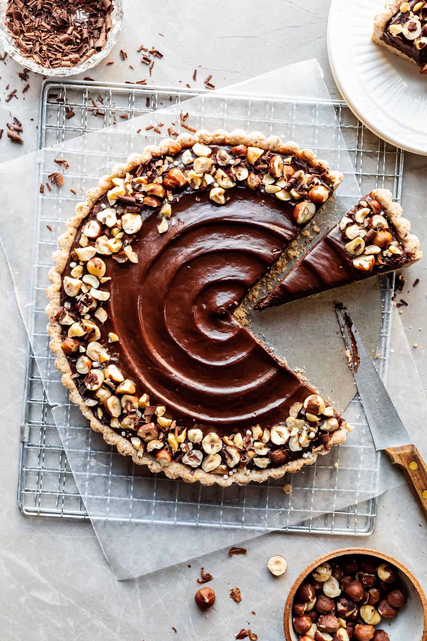 flatlay of vegan chocolate tart garnished with hazelnuts and a slice just cut with a wooden handled knife