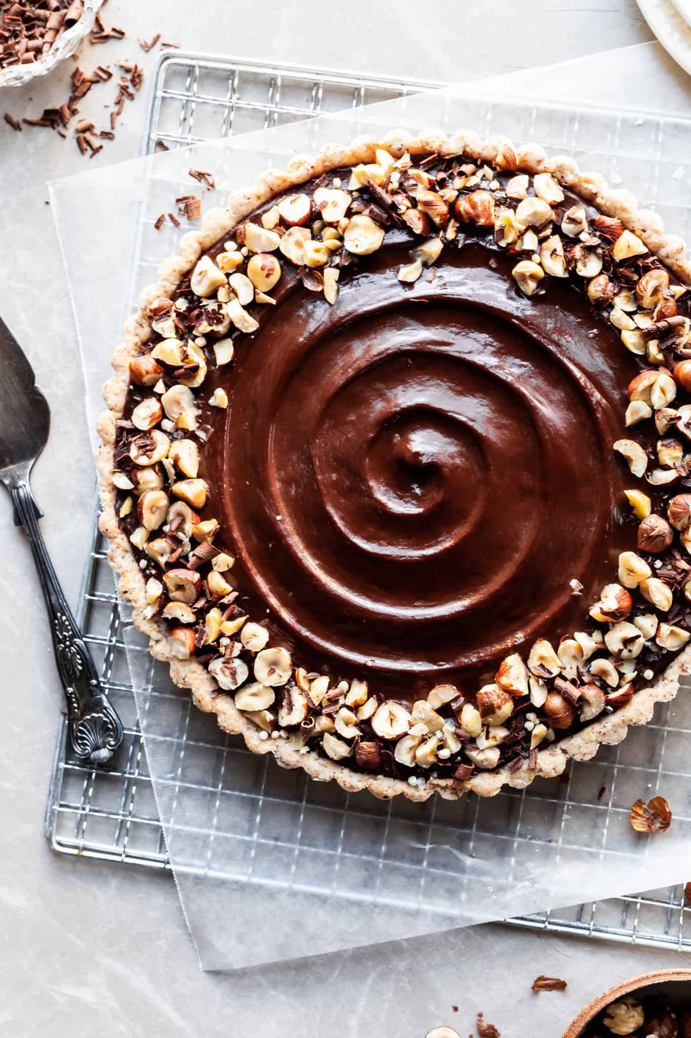 Cropped flatlay of a chocolate hazelnut tart so ⅛ of the tart is not visible. Beside the tart is an antique serving spatula
