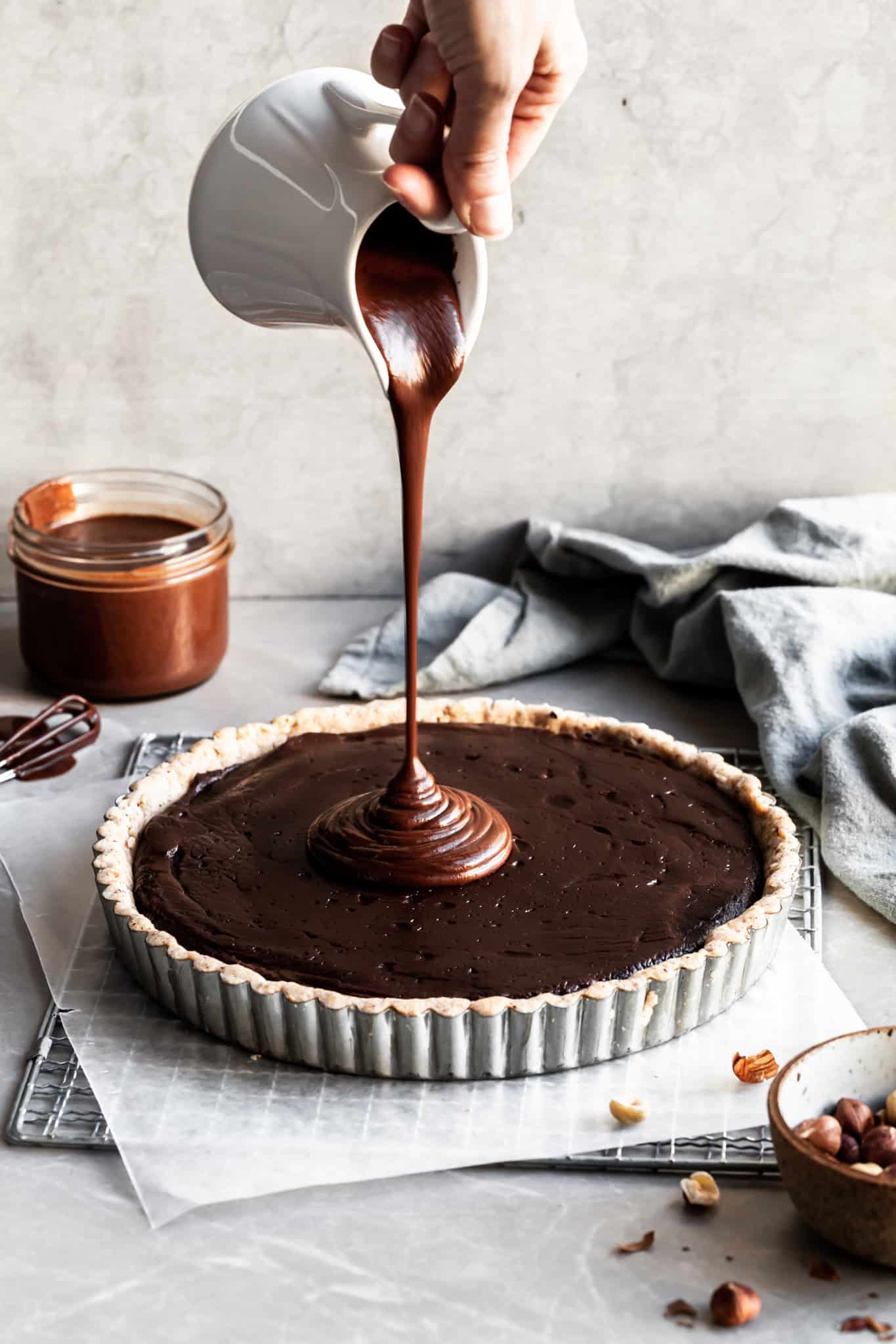 Ganache being poured from a white jug over a chocolate tart