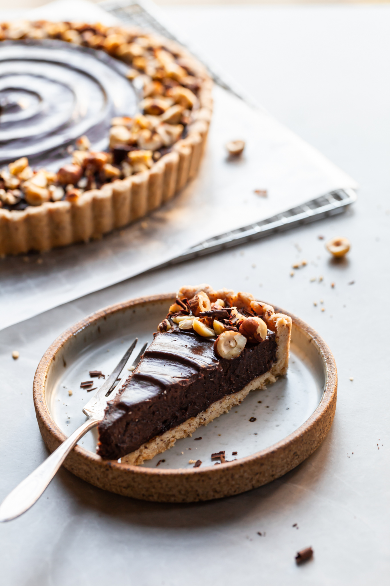 Side view of a slice of vegan chocolate hazelnut tart with the tart in the background