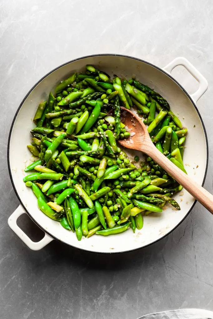 Flat lay of asparagus and peas in a white enamel skillet