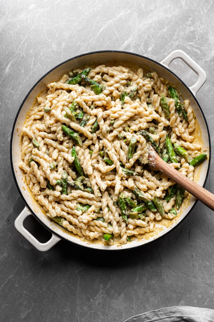 Flat lay of creamy lemon pasta with asparagus and peas in a white enamel skillet