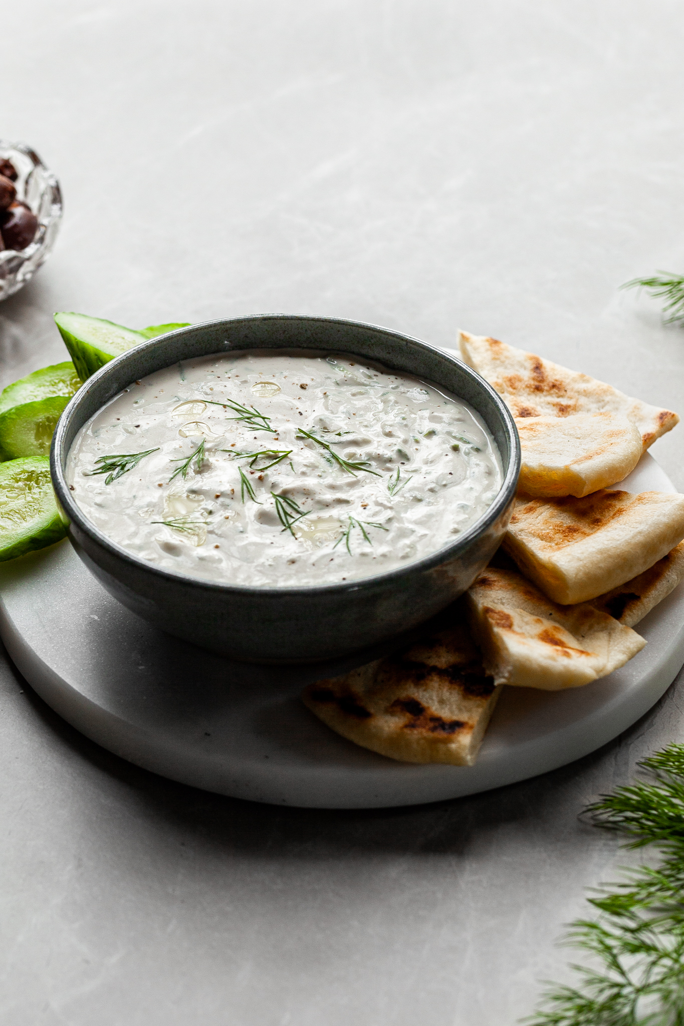 vegan tzatziki in a bowl served with flatbread and a small bowl of olives in the background