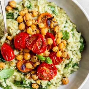 Close up view of a bowl of pesto risotto topped with roasted tomatoes and chickpeas
