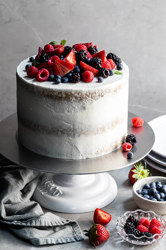 White layer cake with a naked crumb coat, covered in a variety of summer berries.