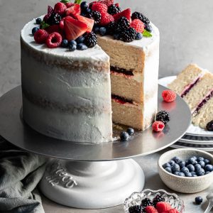 Triple layer vanilla cake layered with fruit filling with a slice cut. A plate in the background with the cut slice of cake.