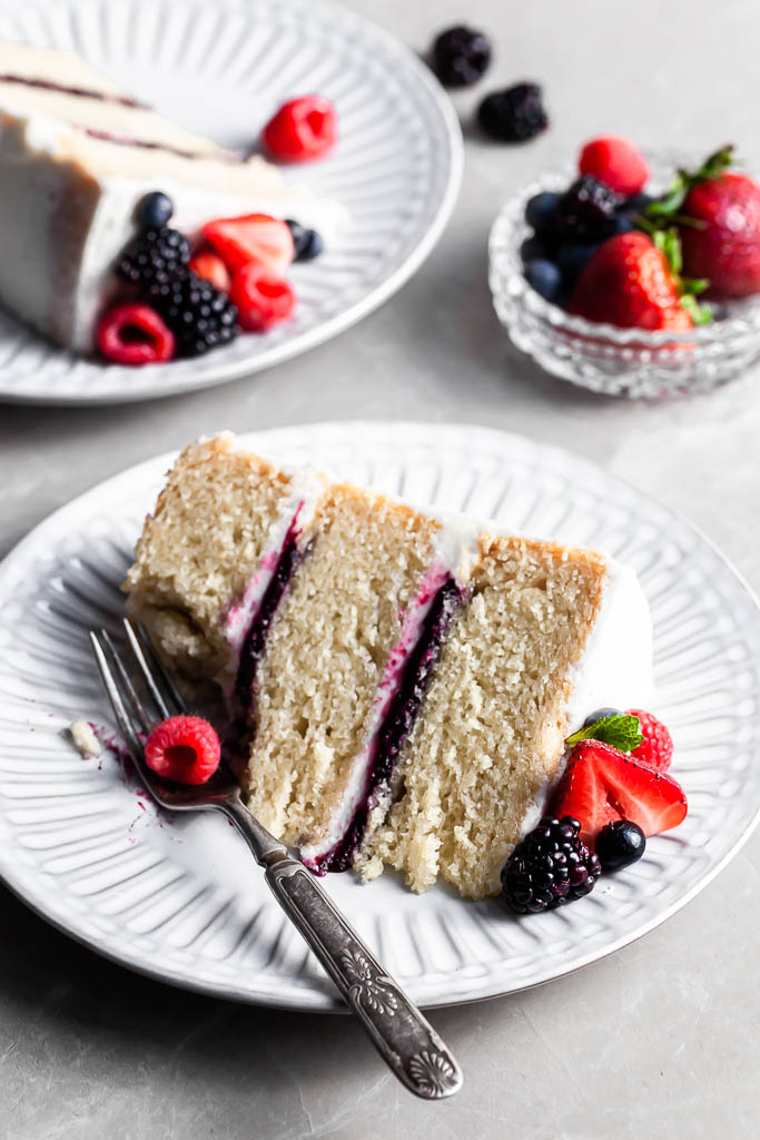 Slice of berry vanilla cake on a white plate with a fork, and a bite missing