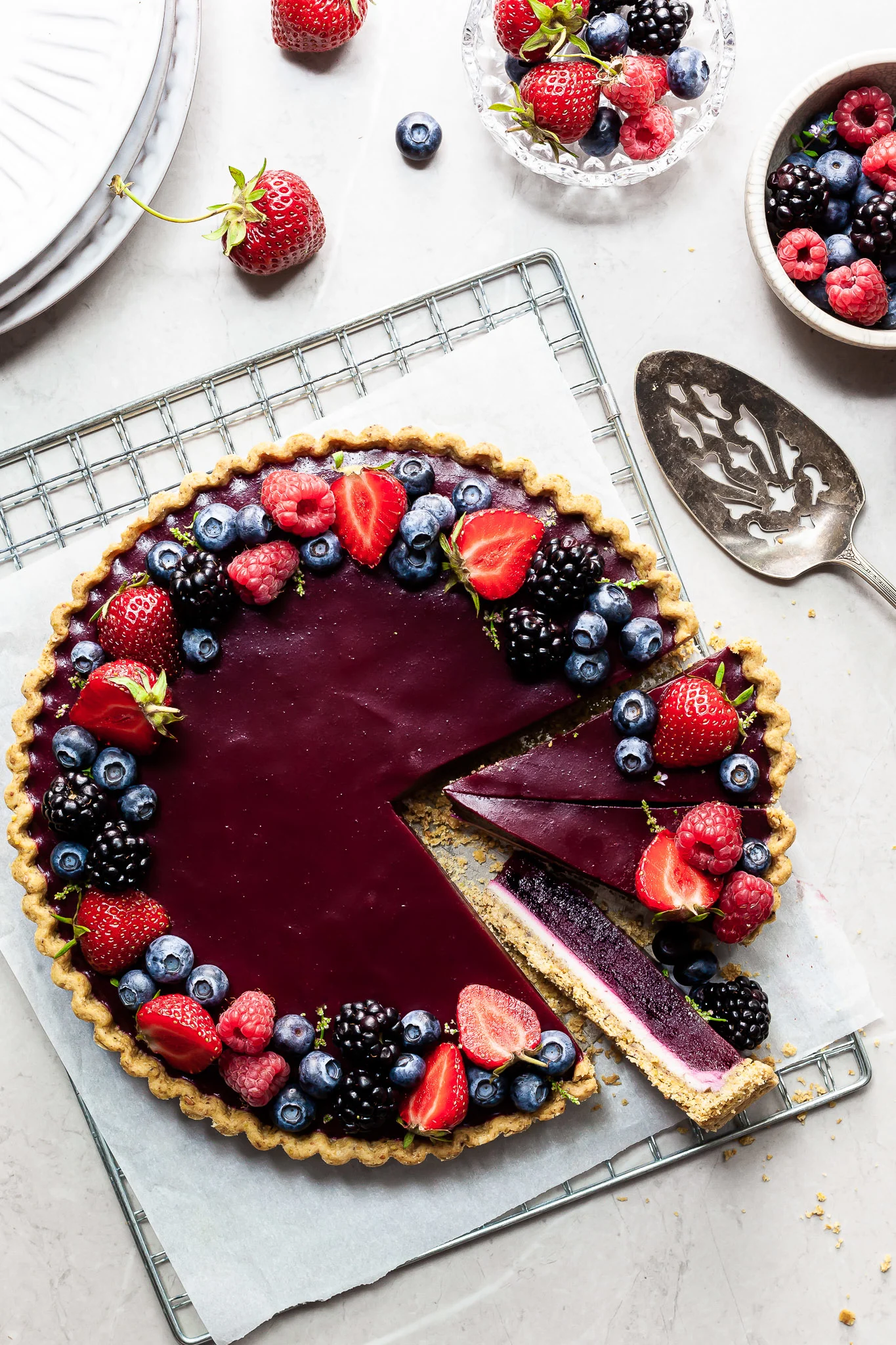 Flaylay of a purple tart with shortbread crust covered in summer berries. 3 slices are made with one on its side revealing the white chocolate ganache on the bottom.